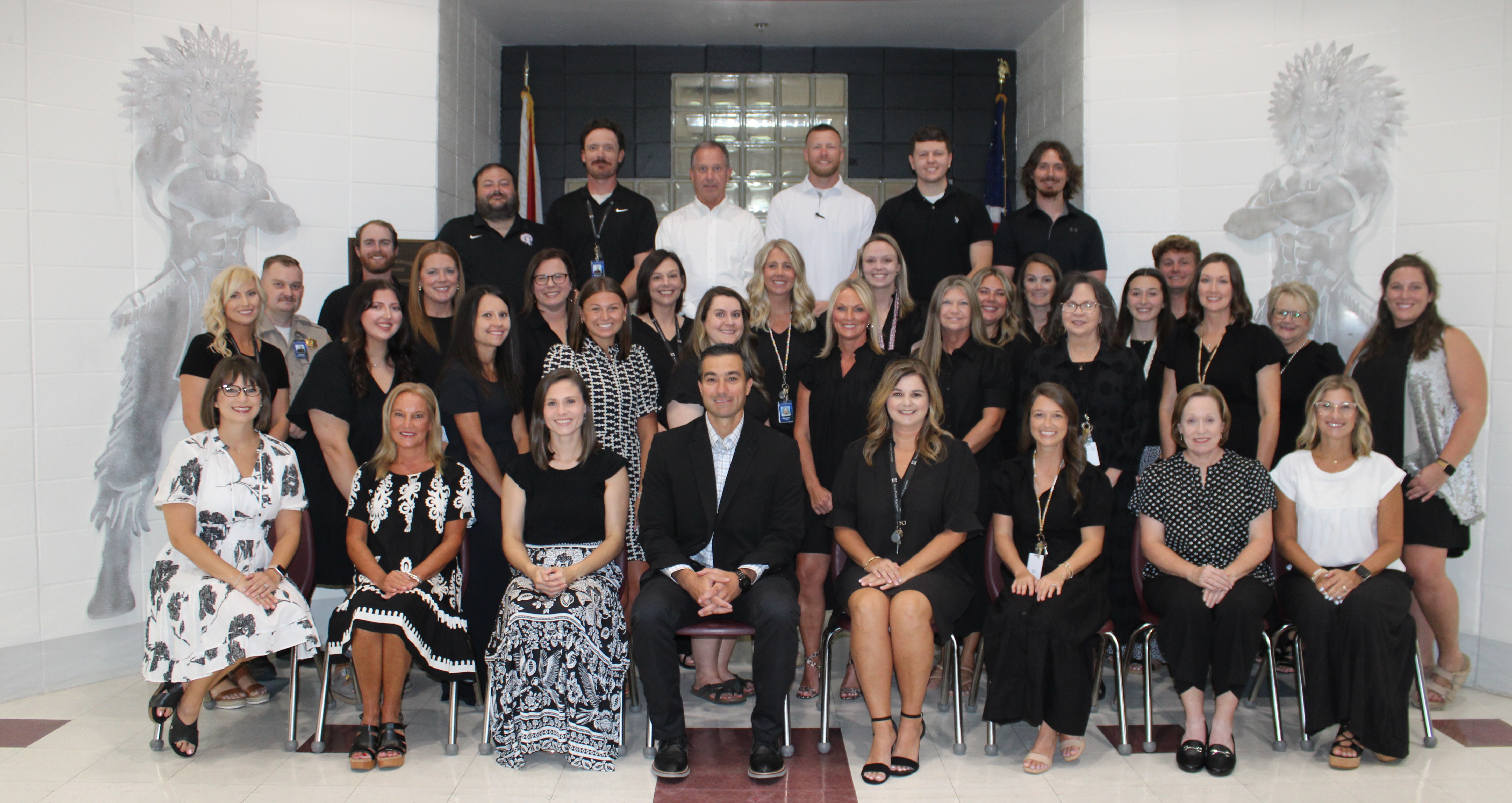 A group of people in black attire posing for a photo in a room with white walls.