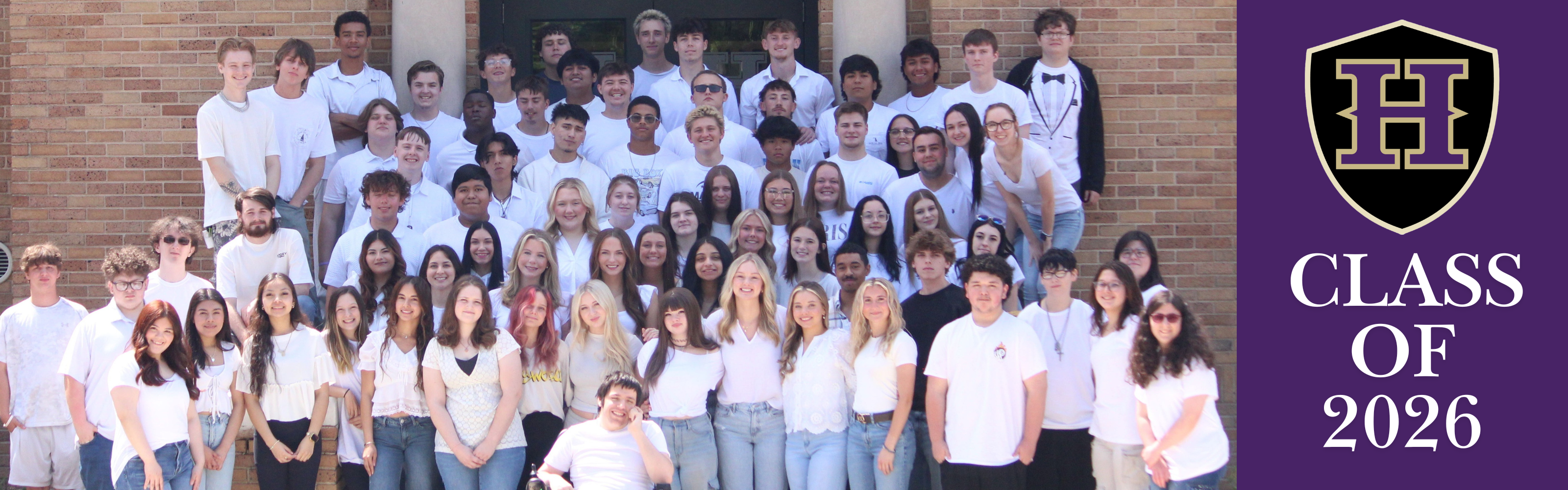 A group of individuals in white shirts and jeans pose for a photo outside a brick building.