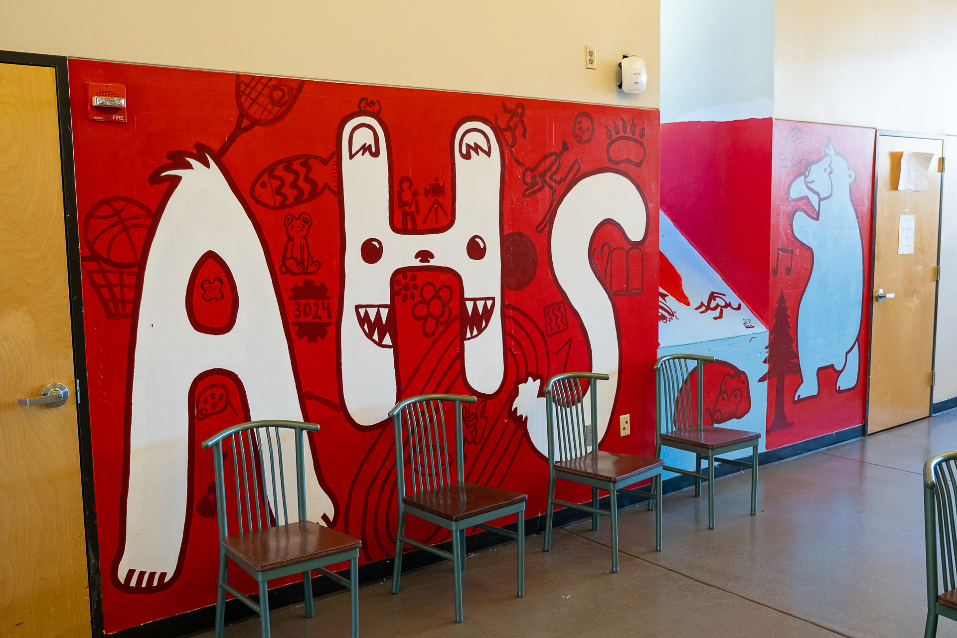 School Mascot Art: A large, bold mural of a school mascot in vivid red tones, providing a dynamic backdrop to a cafeteria setting.