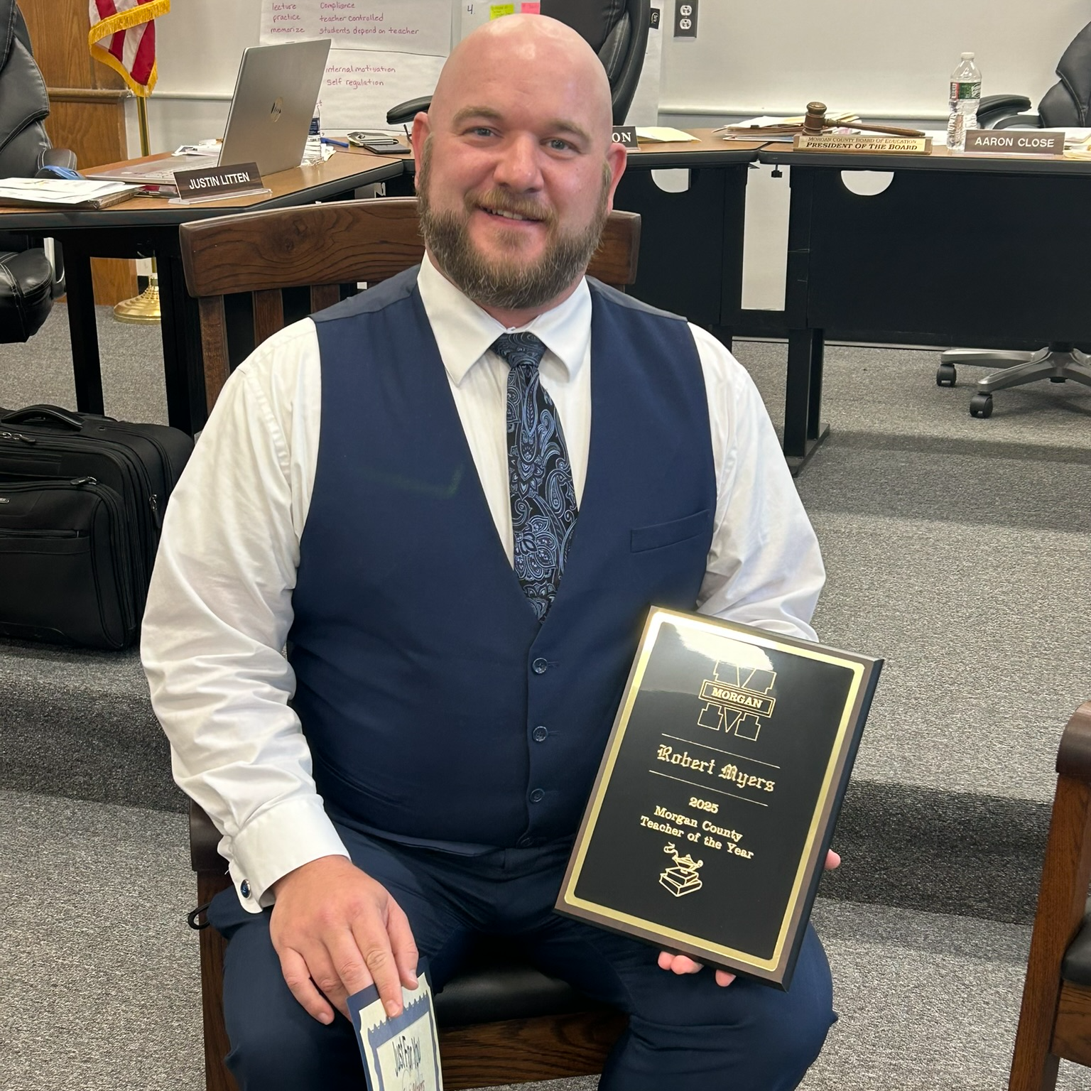 Robert Myers holding a '2023 Morgan County Teacher of the Year' plaque, smiling in a meeting room.