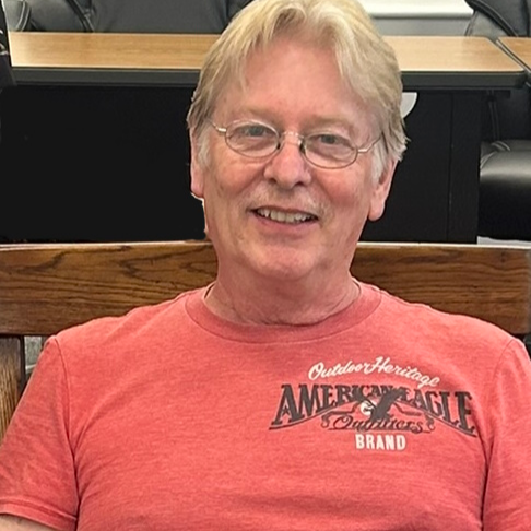 Smiling older man with glasses, blonde hair, and a red shirt.