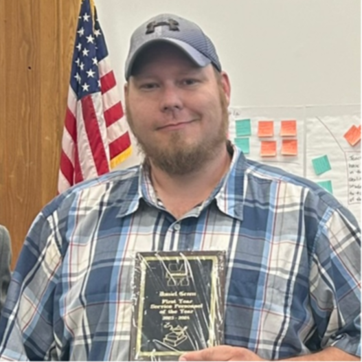 Man in a plaid shirt and baseball cap holding an award.