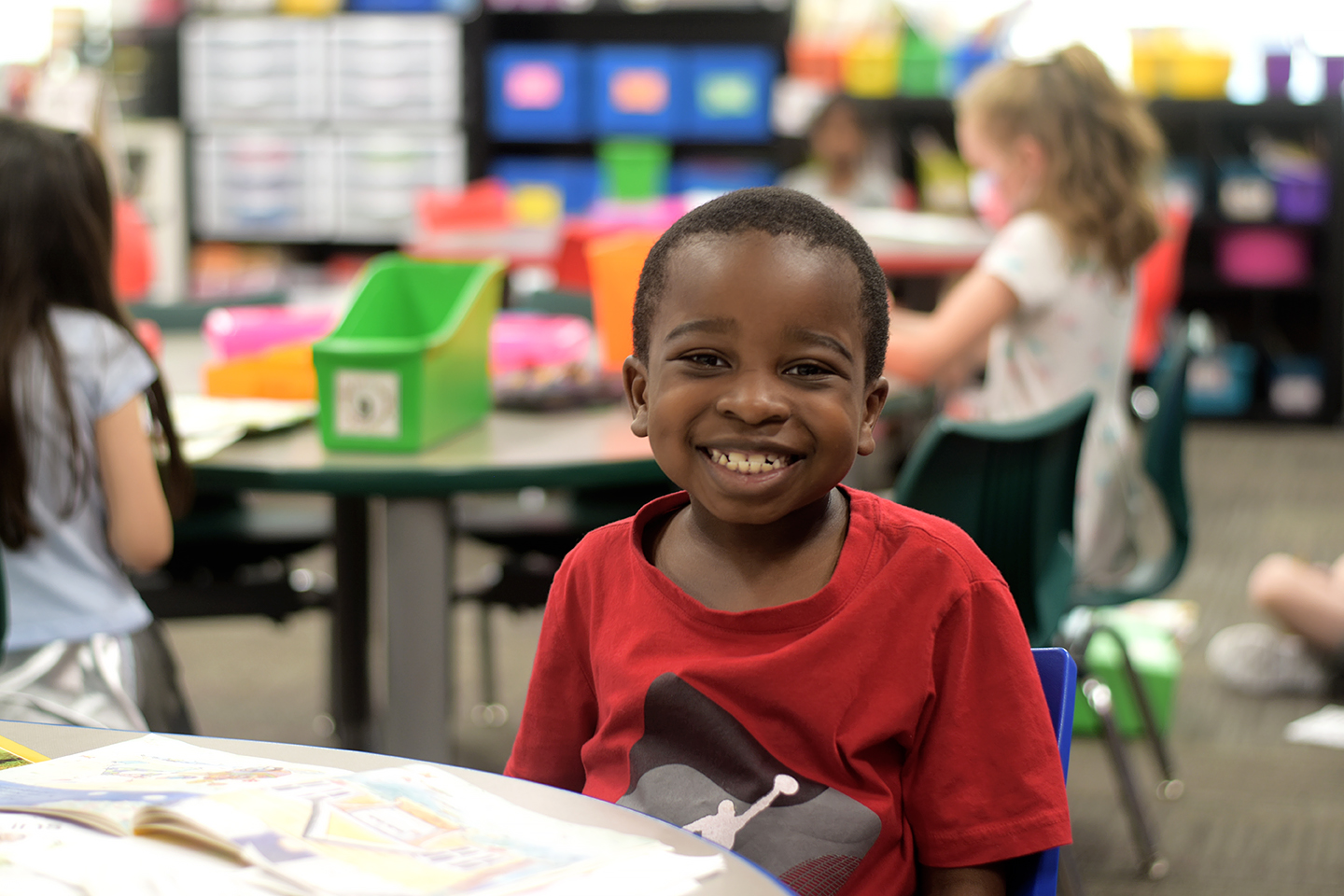 Elementary student sits at his desk with a big smile on his face
