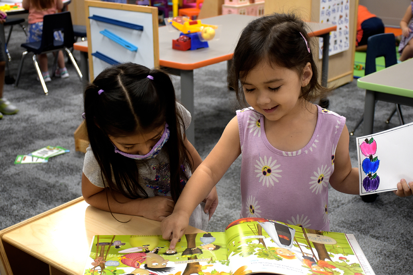 Pre-K students read a book; one student points to an image on the page