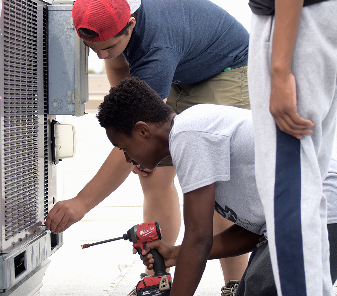student uses drill to repair air conditioning unit