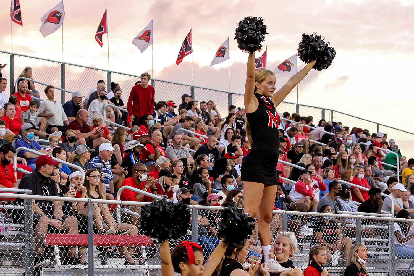 Cheerleaders at home football game with crowd in stands