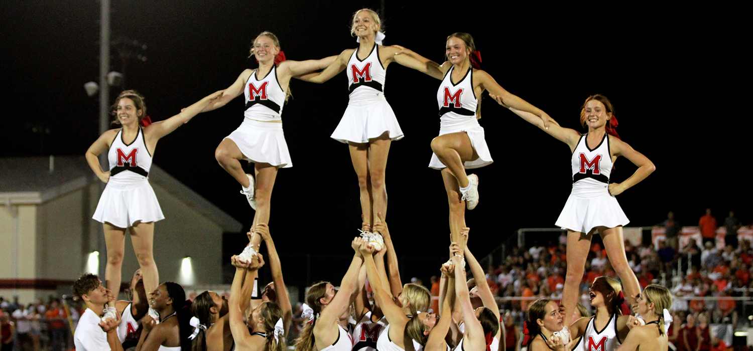 High school cheerleaders perform a stunt at a football game