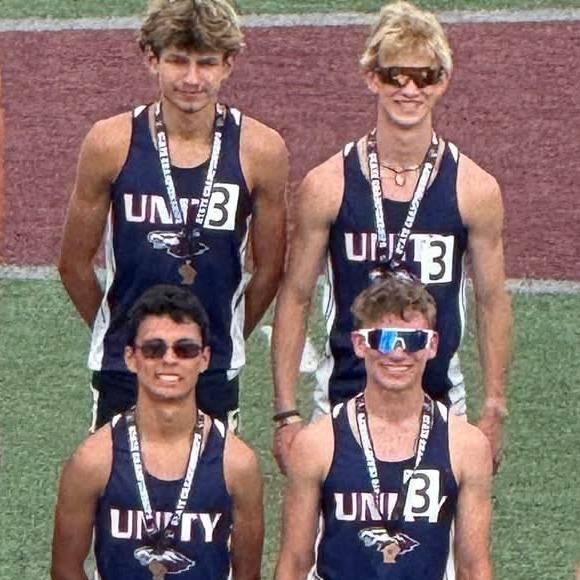 Four Unity track and field athletes posing together with medals on a podium.
