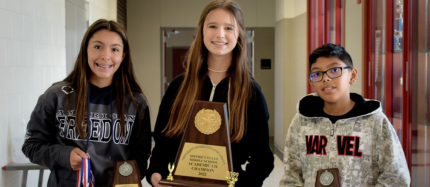 Three students in a hallway holding the school's UIL Academic Championship trophies and medals