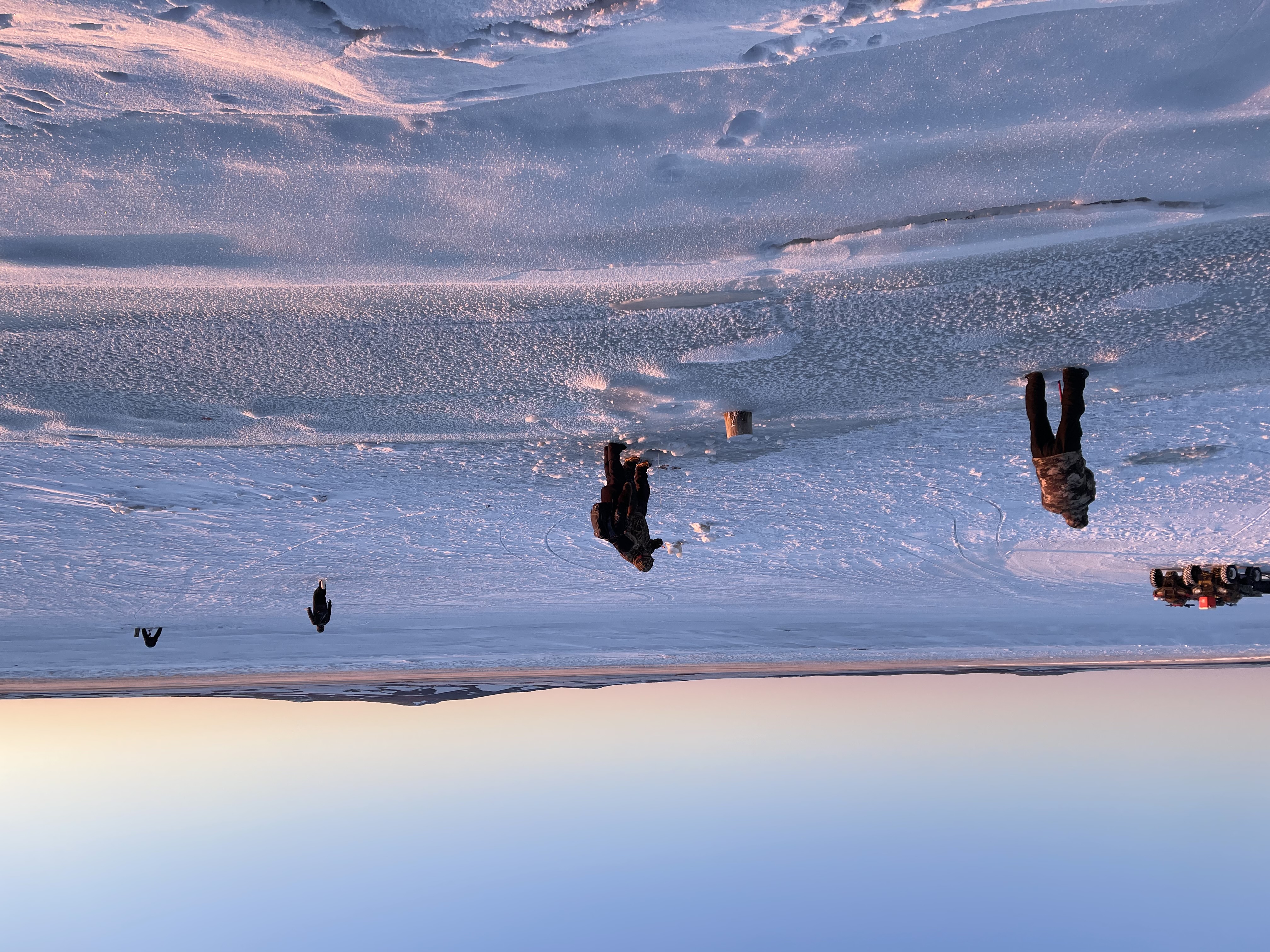 Four people spread out, from near to the horizon, ice fishing.