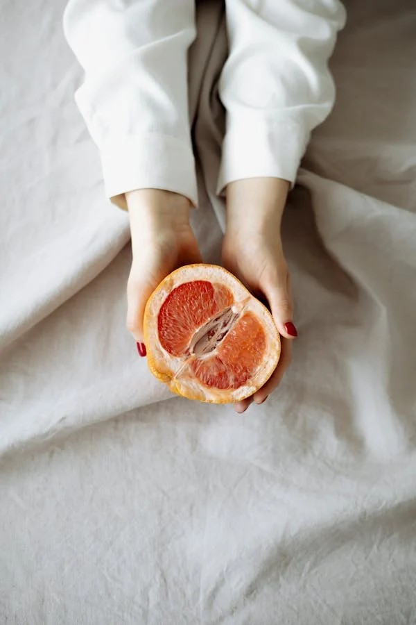 hands with light long sleeves holding a citrus fruit cut in half