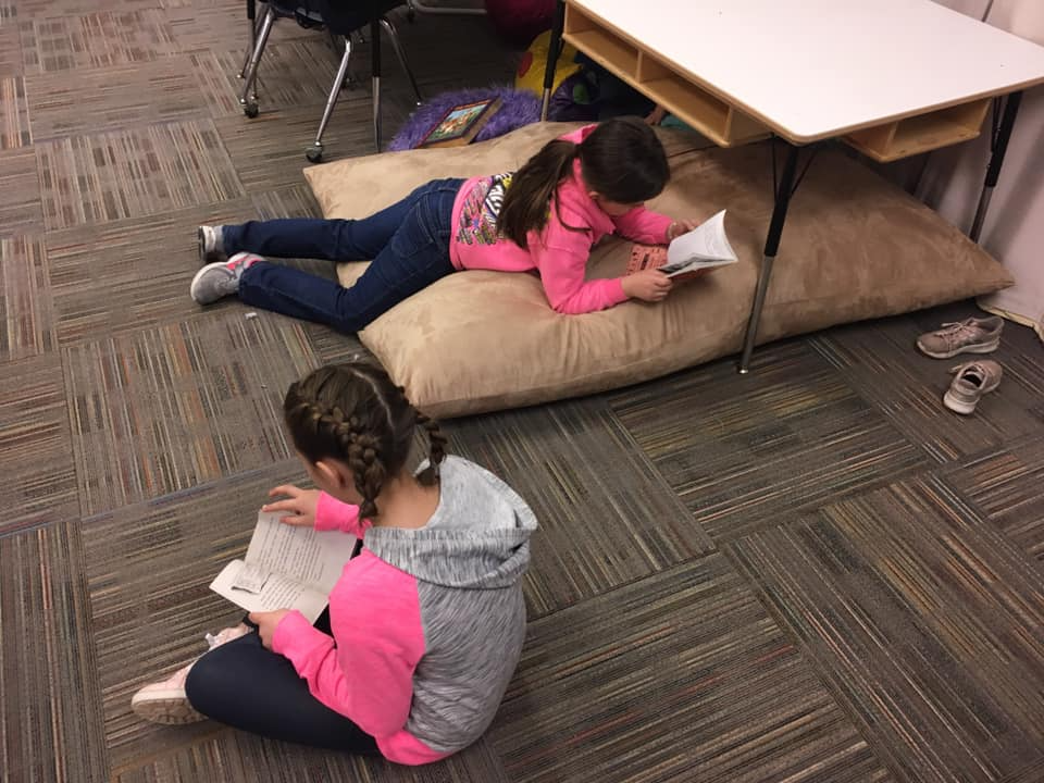 Students sitting on the floor reading books with braided hair 
