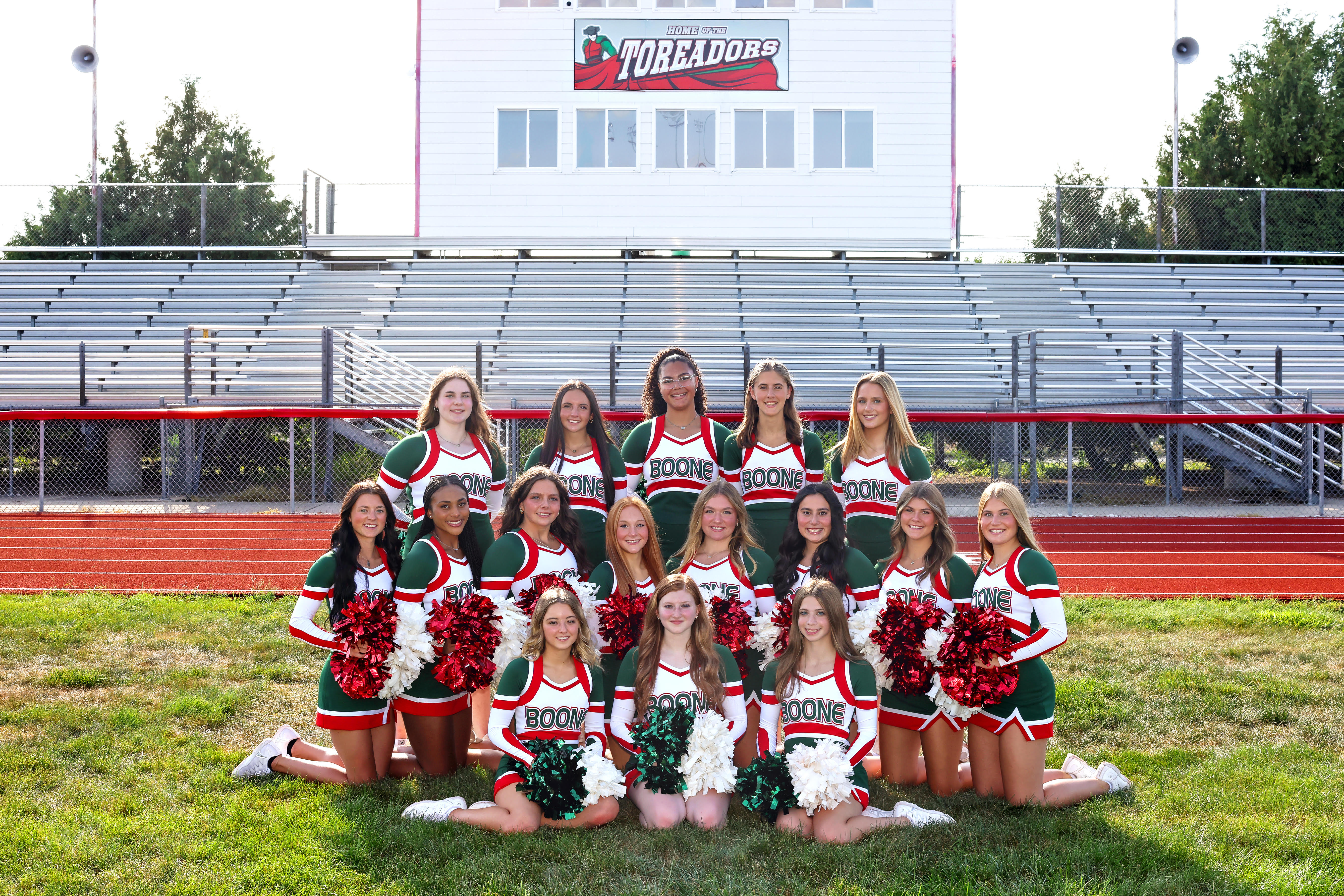 Football Cheerleading students on the track with bleachers in the back