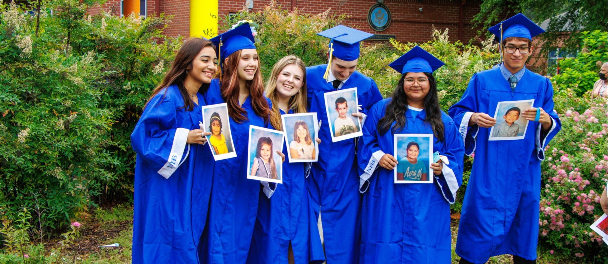 High school graduates post with their children pictures outside in their caps and gowns.