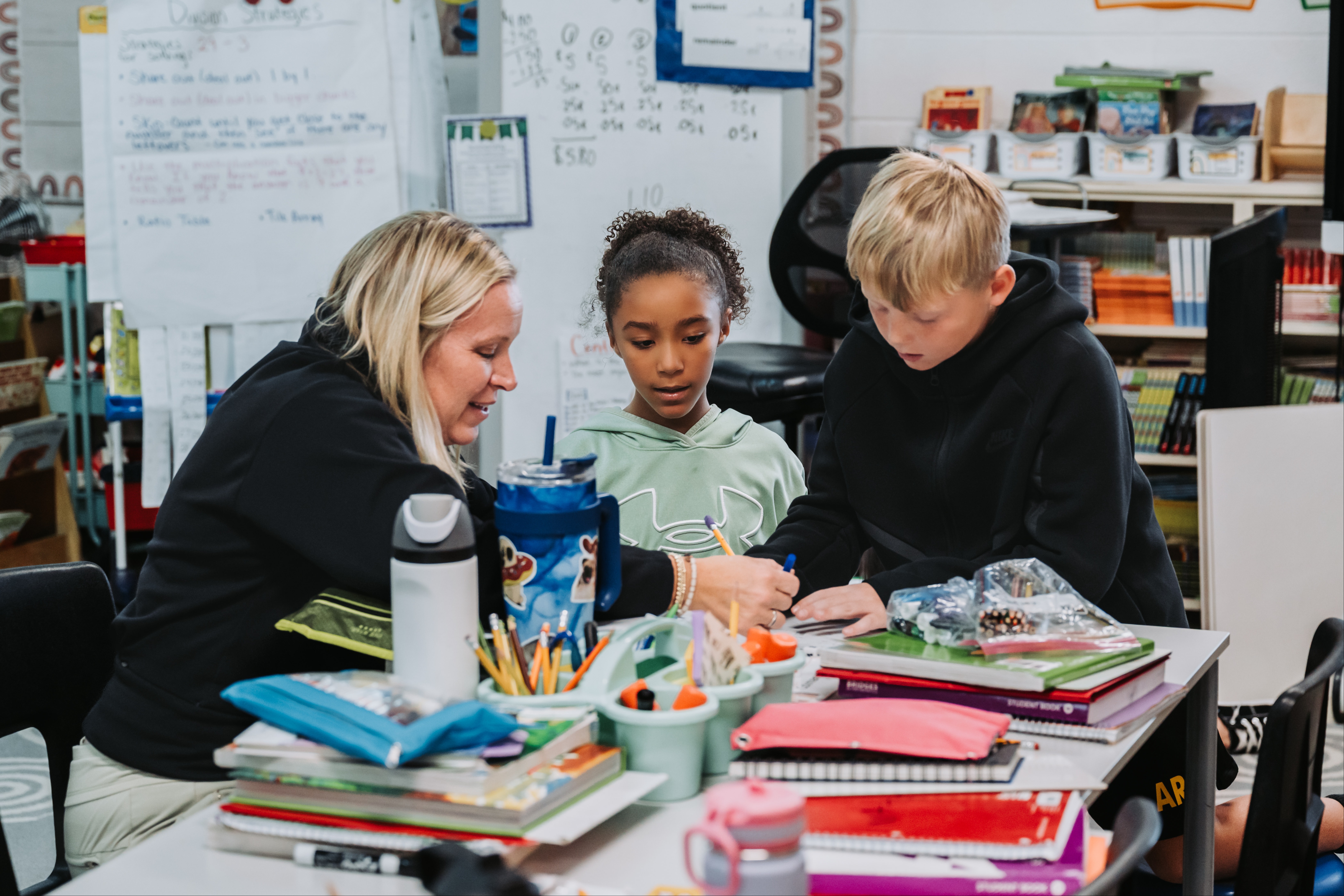 Two students sit with teacher working at a desk.