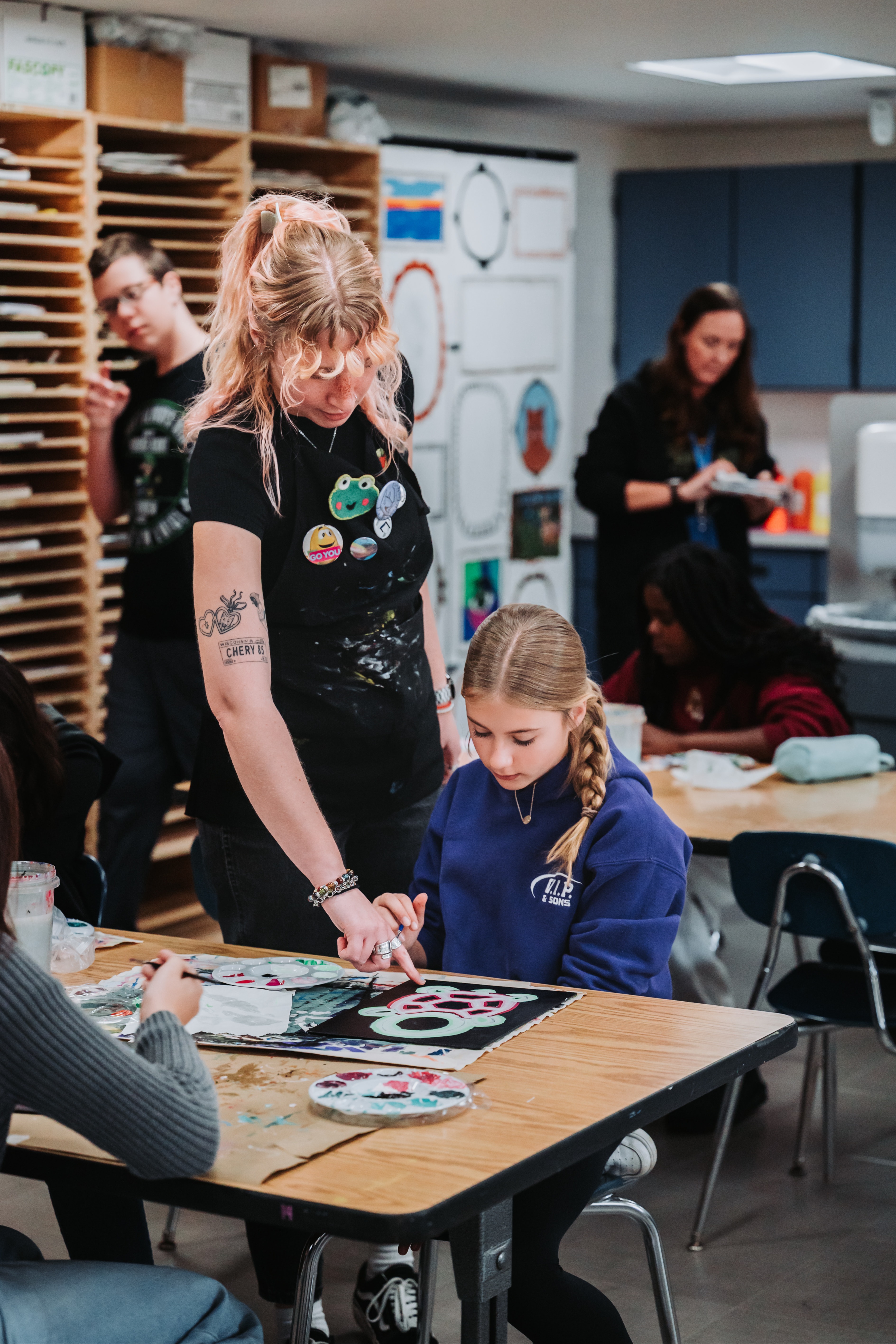 A teacher connects with a student at a table on a project.