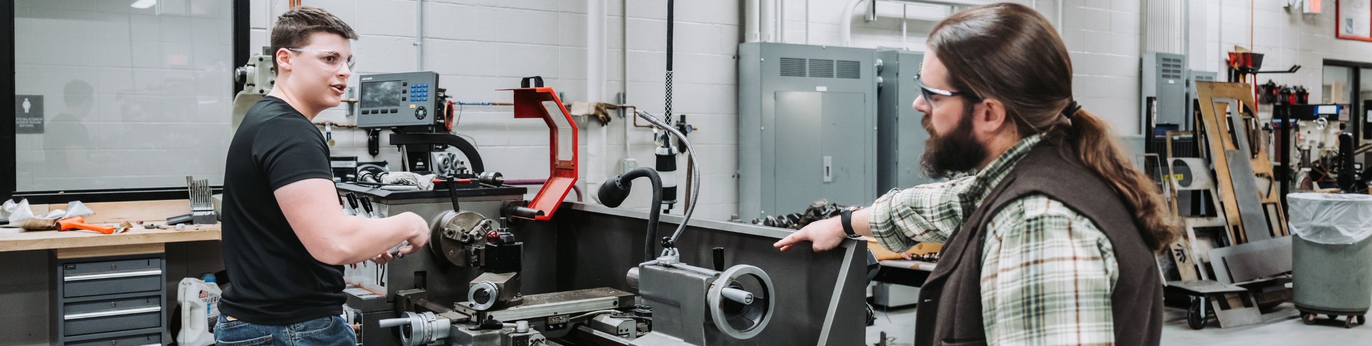 While working on a machine, a student chats with teacher.