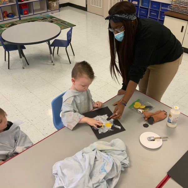 Students assisting preschooler with art assignment