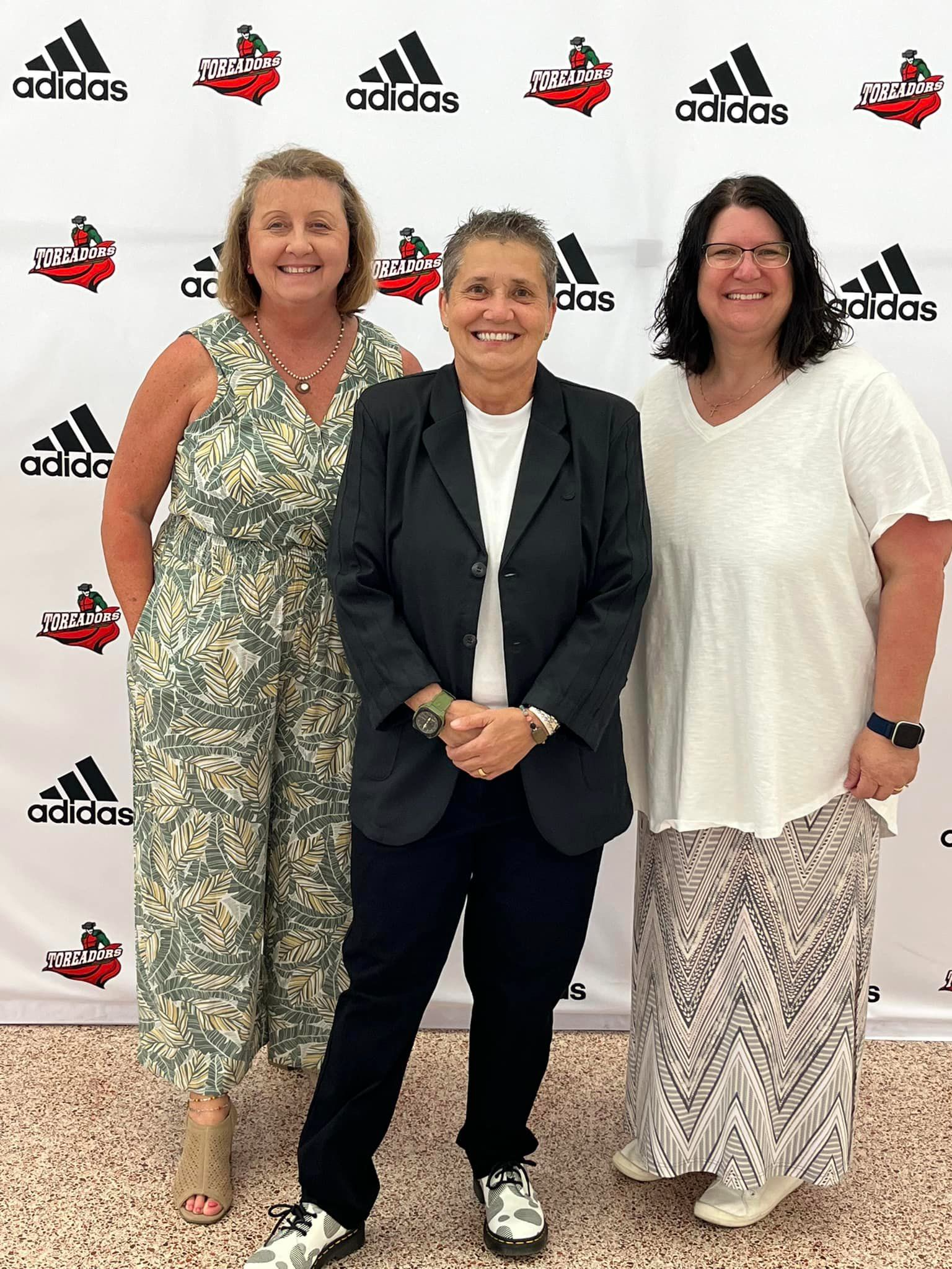 3 staff members standing in front of the Toreador and adidas logo banner 