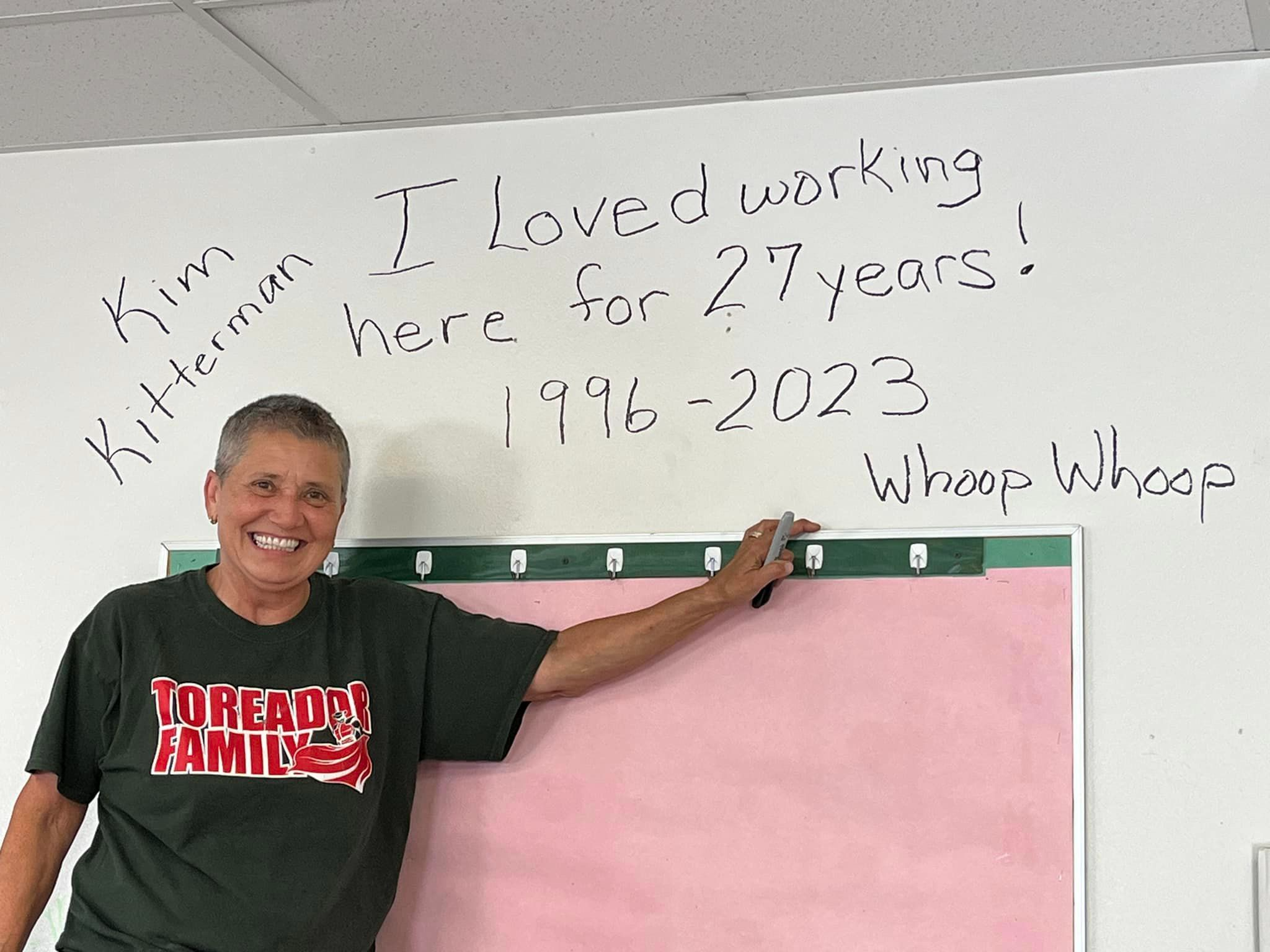Director Kim Kitterman standing at a wall where it reads: I loved working here for 27 years 1996-2023 whoop whoop