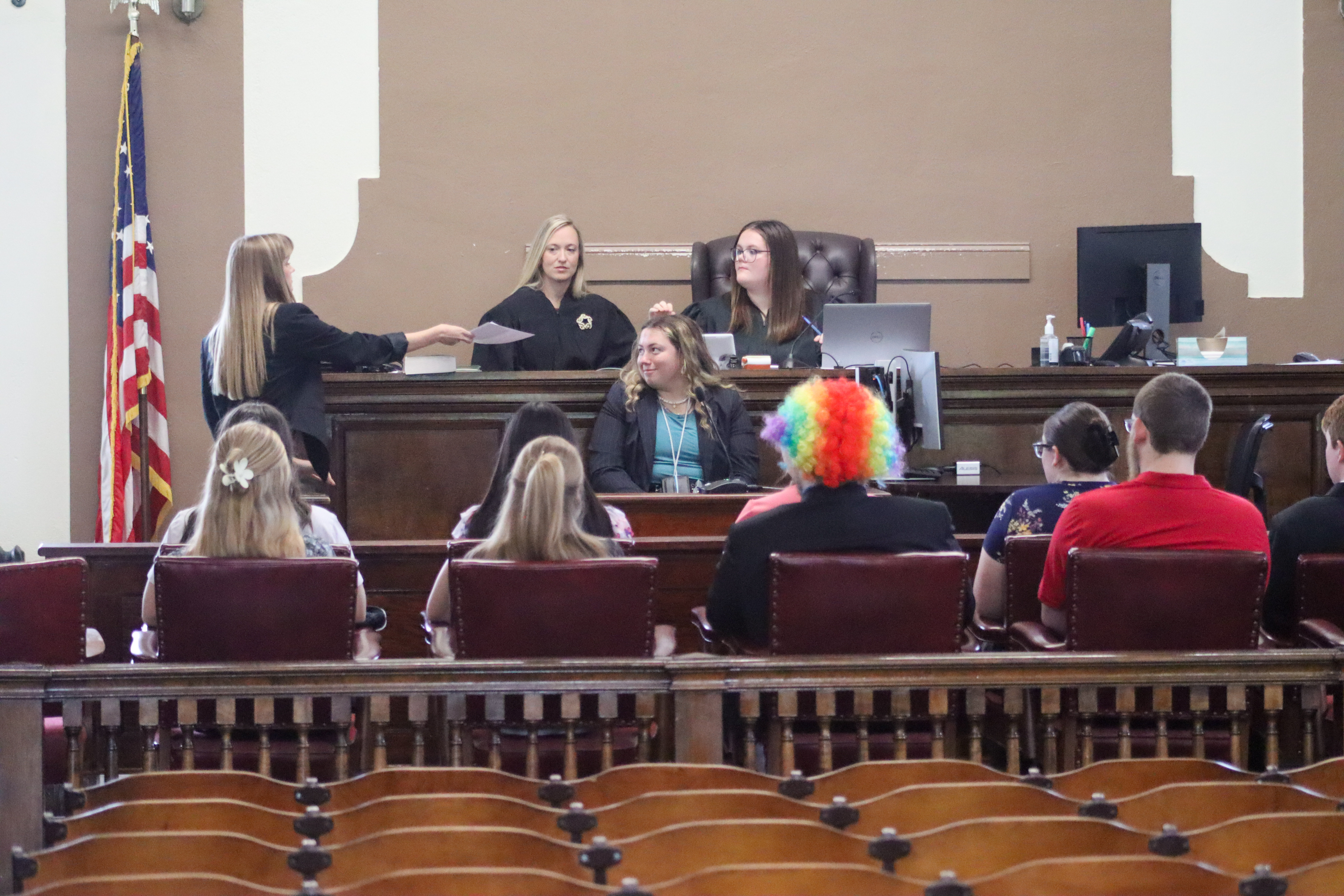 GCHS Mock Trial - students sitting in a jury box. another student handing a piece of evidence to the judge
