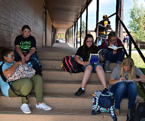 students study sitting on steps outside of school