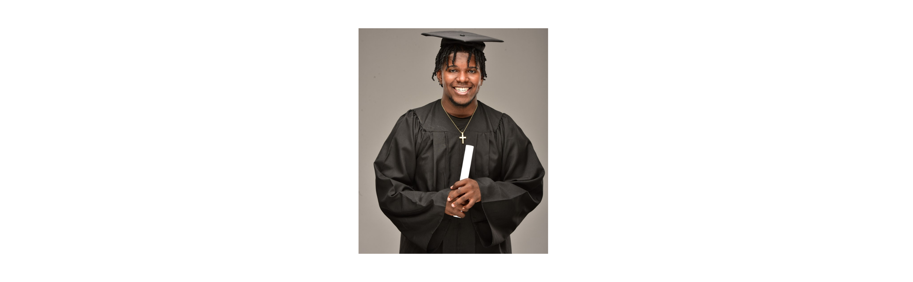 Student wearing his graduation cap and gown. His cap and gown are black.