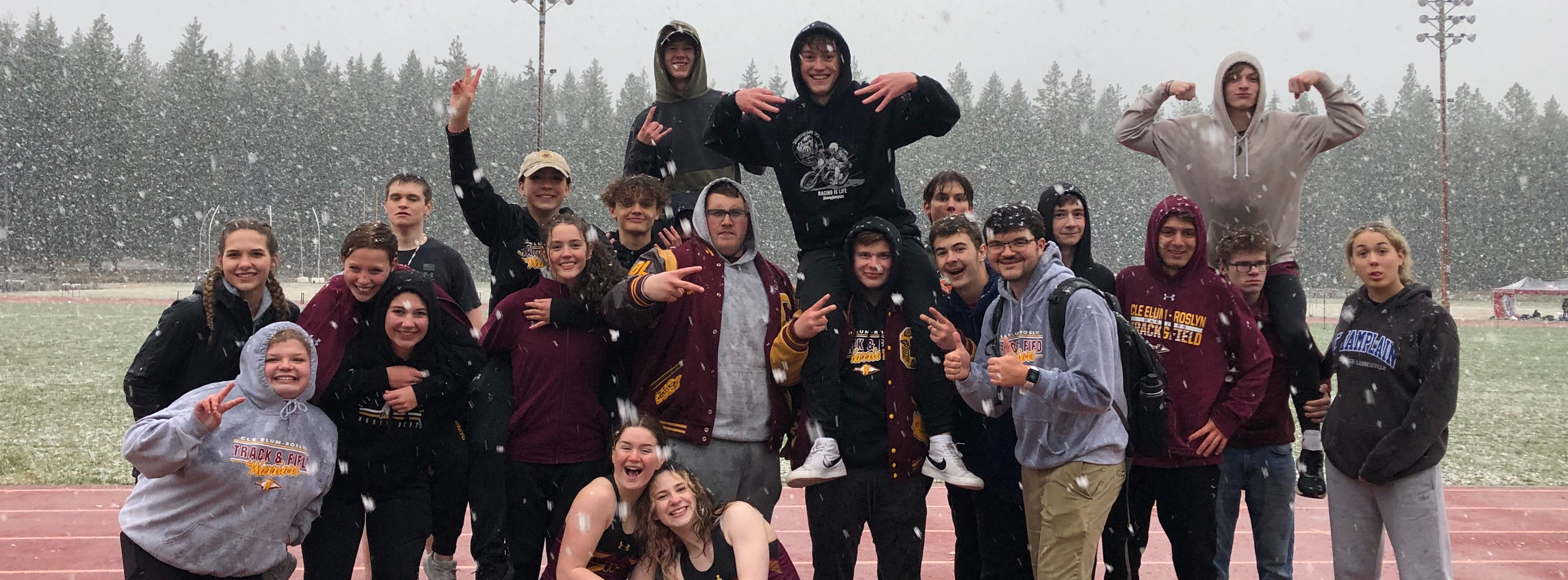 Members of the track team gathered together smiling at the camera during a snow storm at a meet 