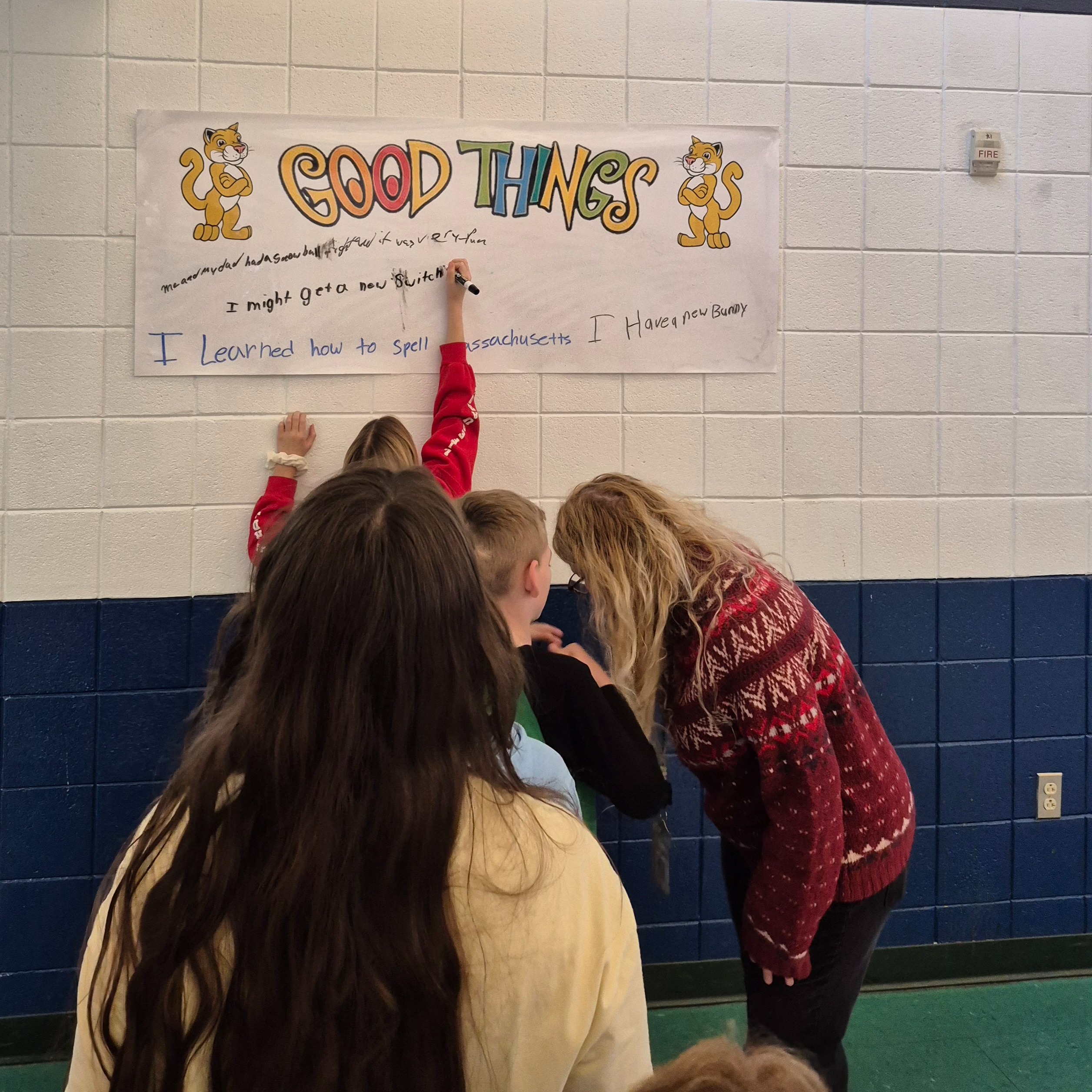 Students and adults lined up to write on a poster which say "Good Things" in large colorful font.