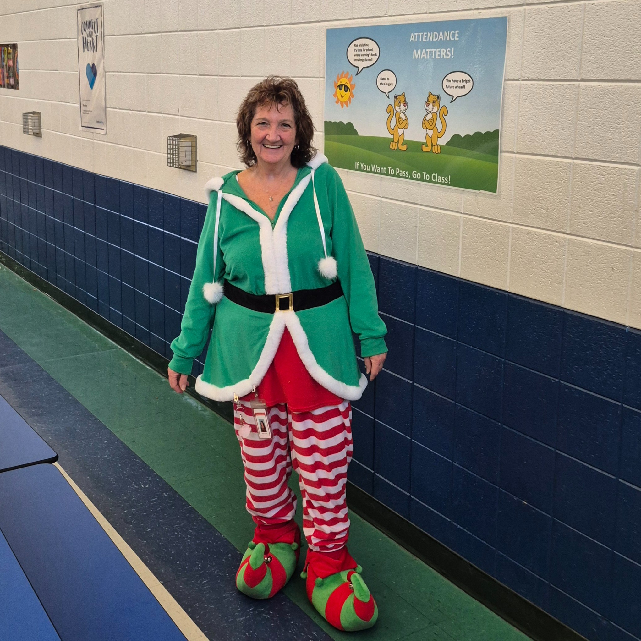 Staff member wearing a festive elf outfit smiles in a school hallway, modeling a joyful attitude that reflects how everyday interactions and positivity help create a welcoming environment for students.