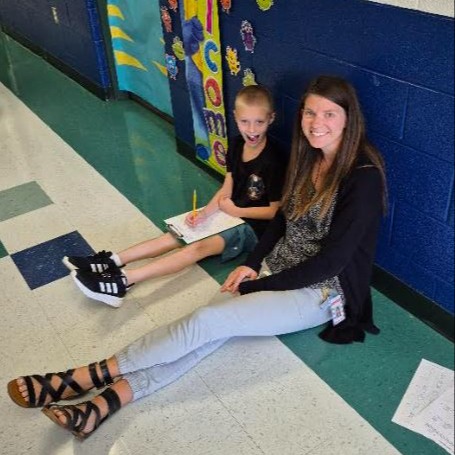 Staff member sits with a smiling scholar working in the hallway.