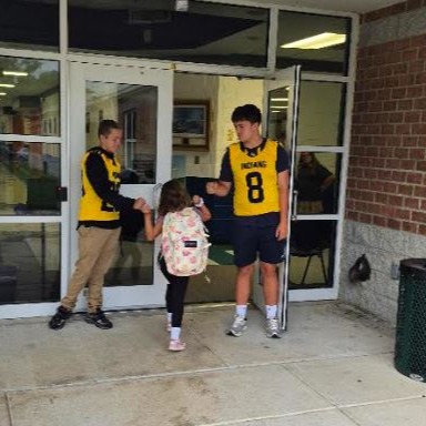 Two high school athletes greet a young scholar at the school entrance.
