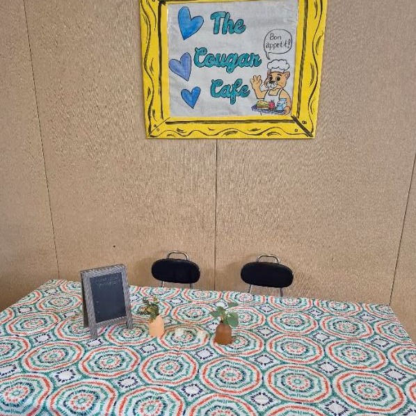 Cougar Café table with chairs, decorations, and a colorful handmade sign.