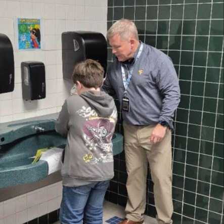 Staff member assists a scholar at a school sink.