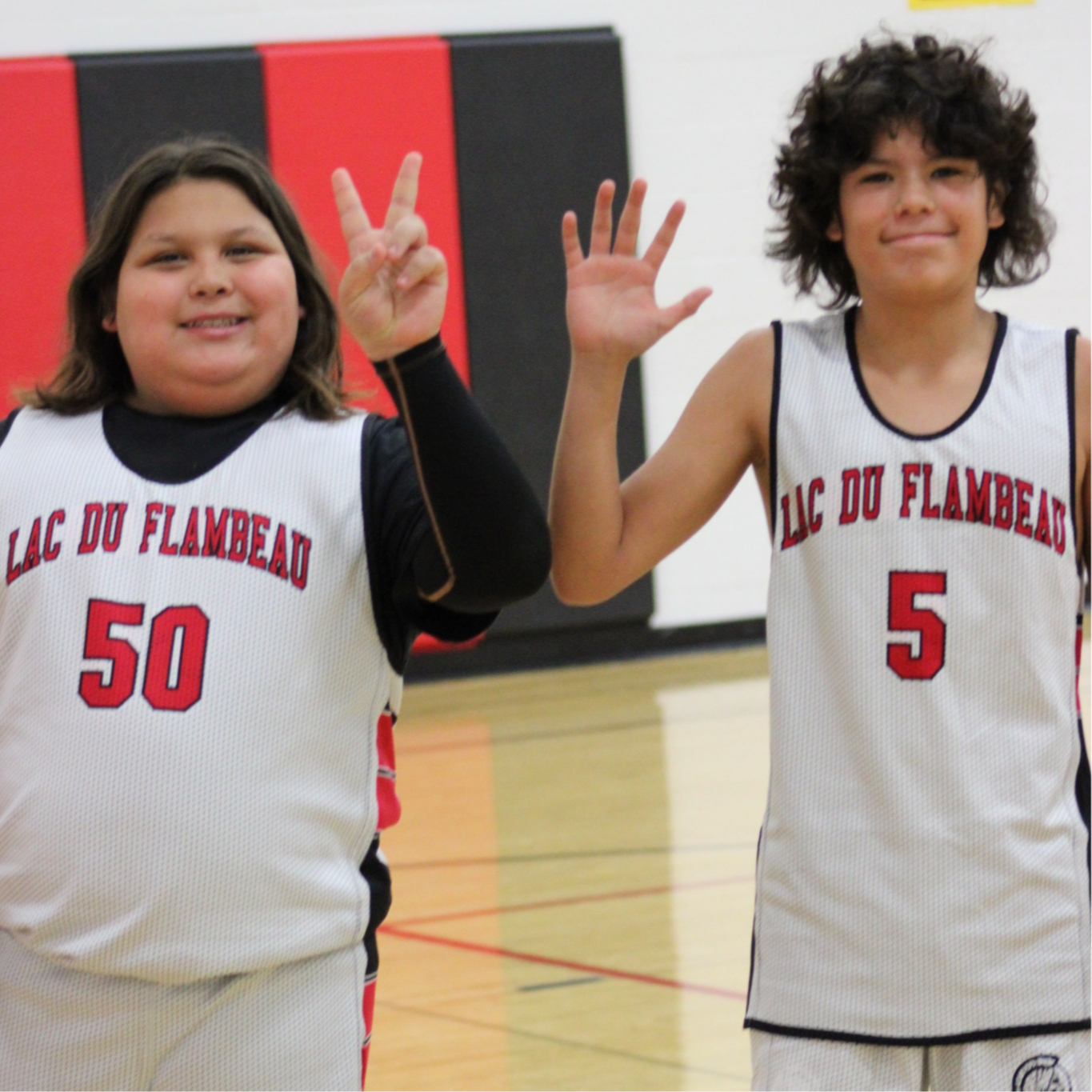 Two basketball players smile and wave at camera