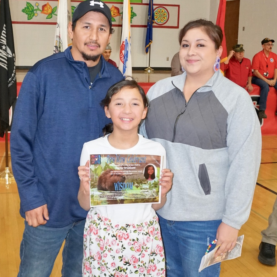 A girl proudly holds a certificate with her two parents posing with her