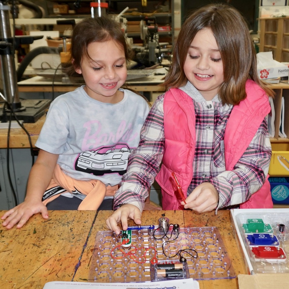 two young girls smile as they work on a science project