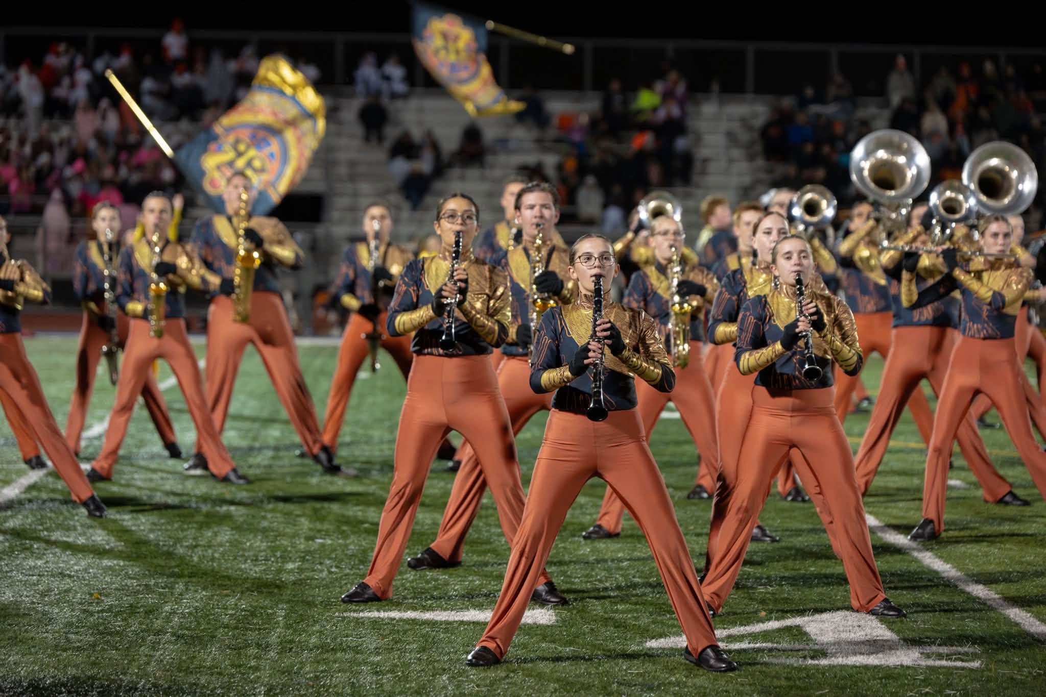 Group of performers in matching uniforms marching and playing instruments on a football field.