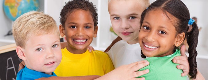 Photo of four young kids all hugging and smiling at the camera