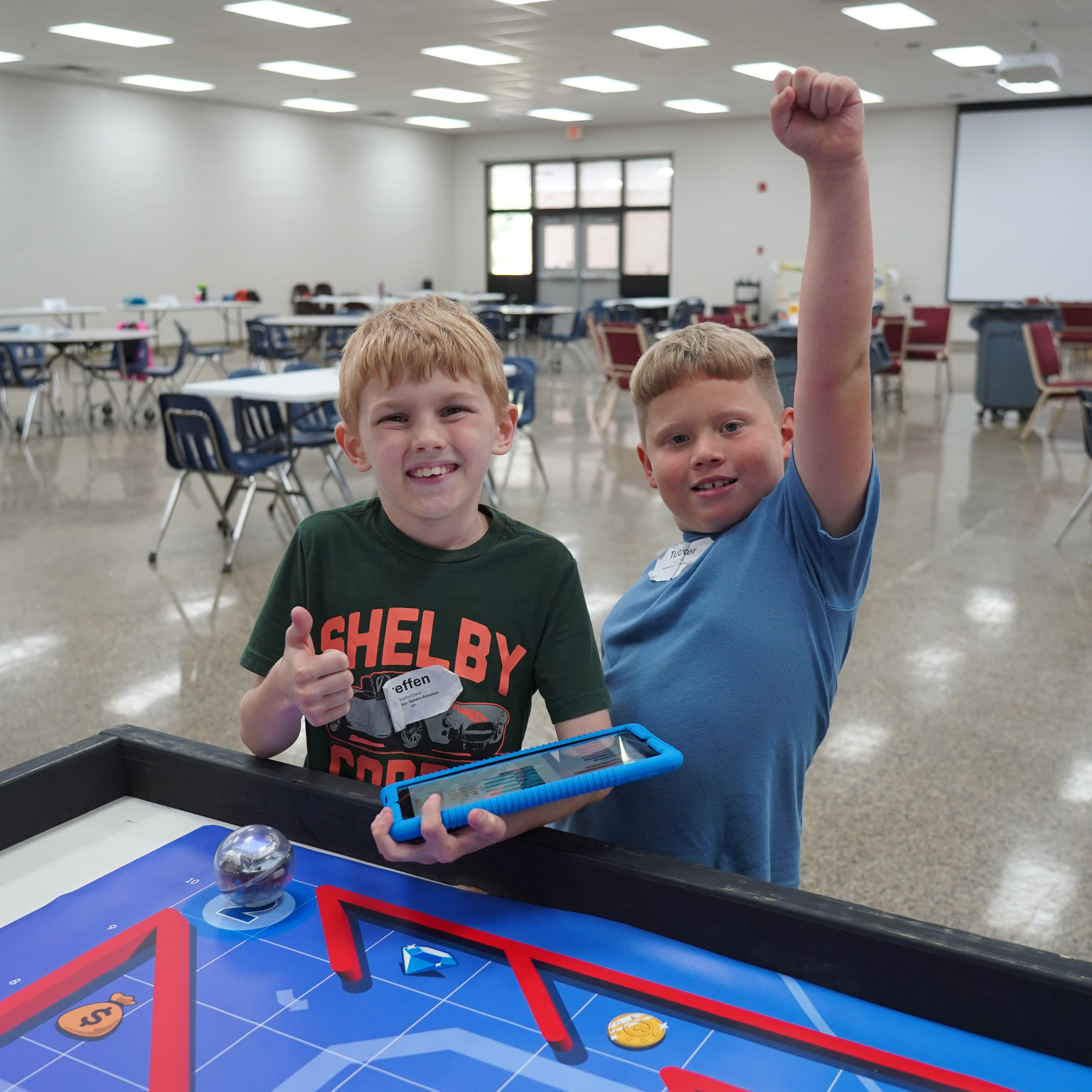 Two children play with a ball in a maze game in a large room. They are smiling.