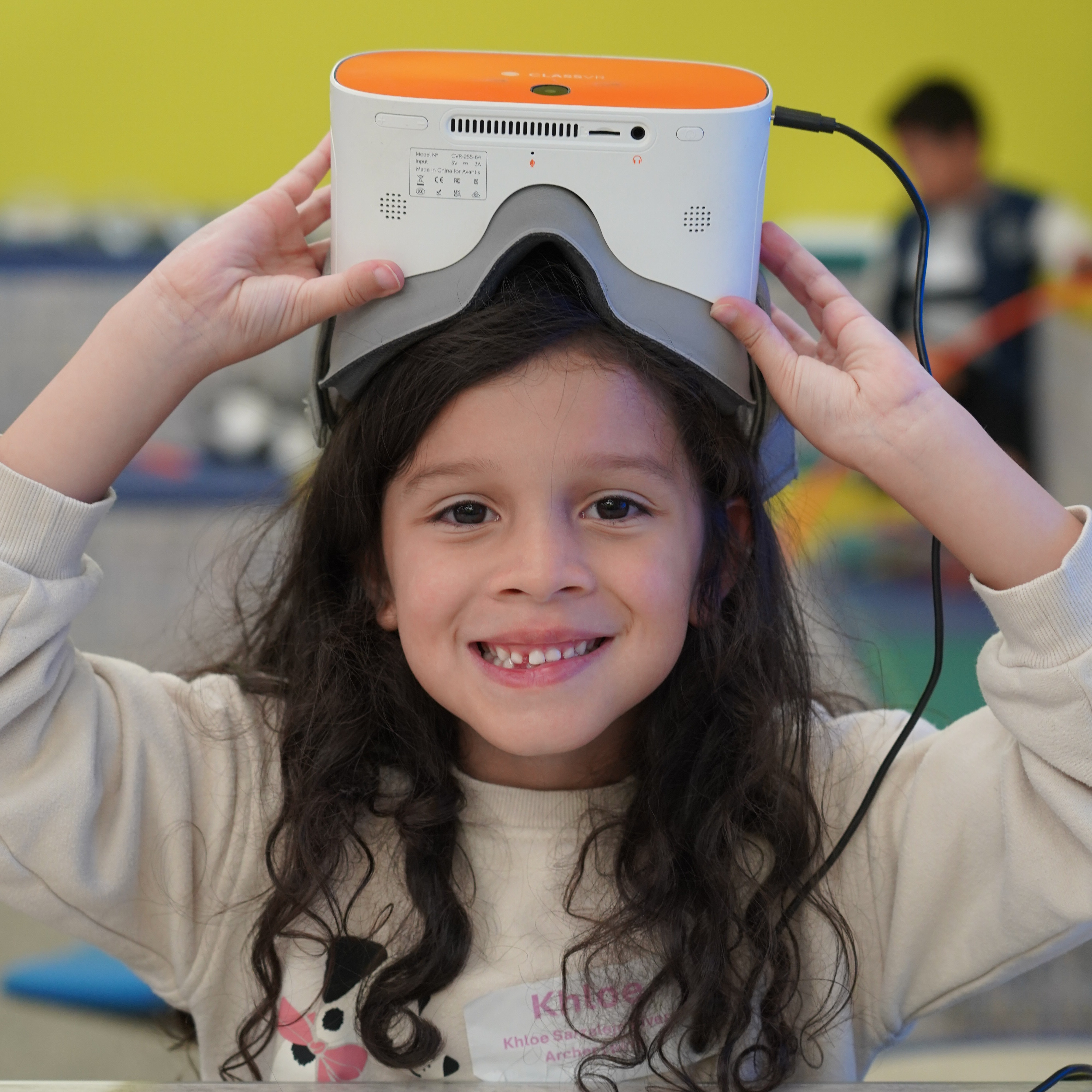 Girl wearing an orange virtual reality device, smiling and holding it on her head.