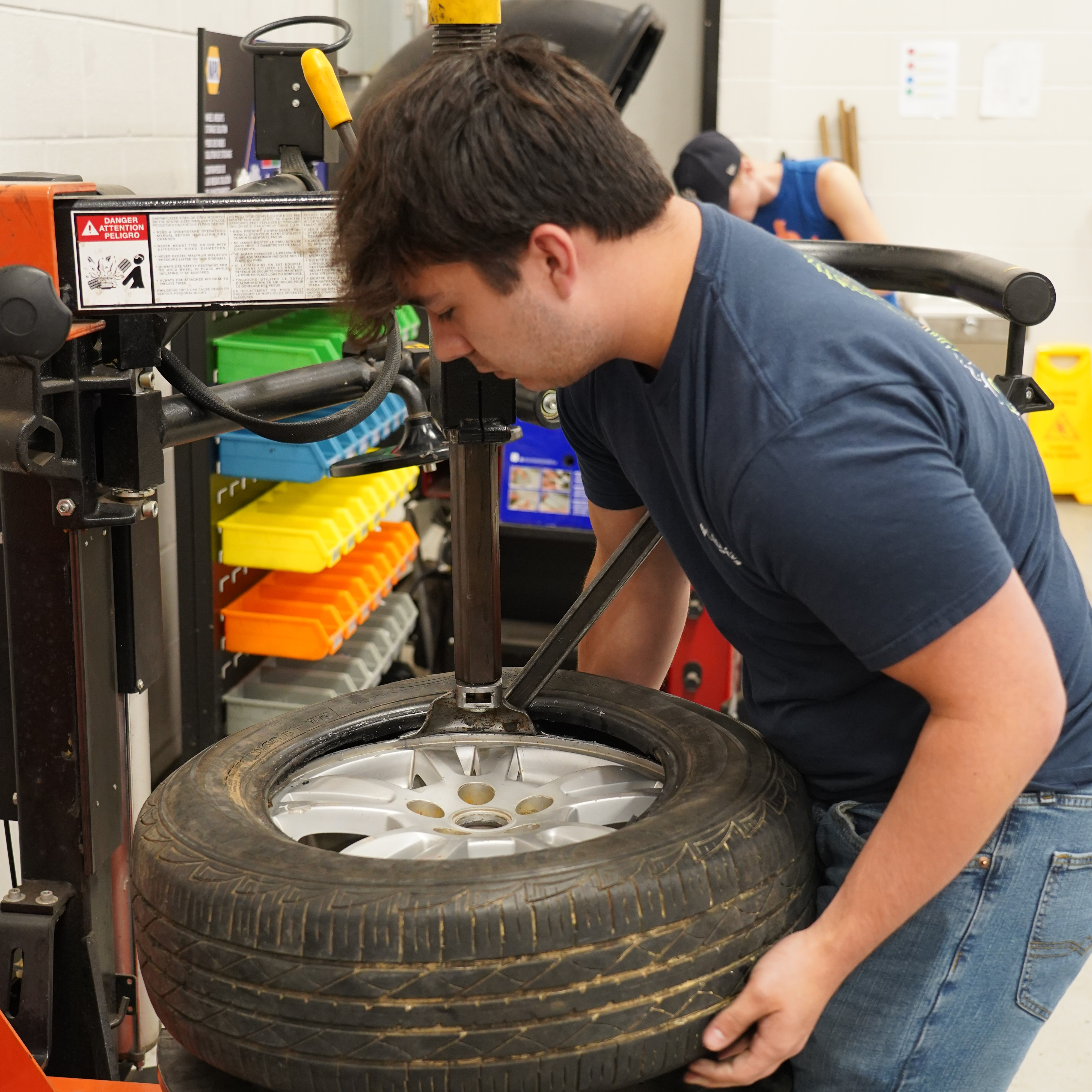 A man is working on a tire using a machine in a room with orange and white walls.