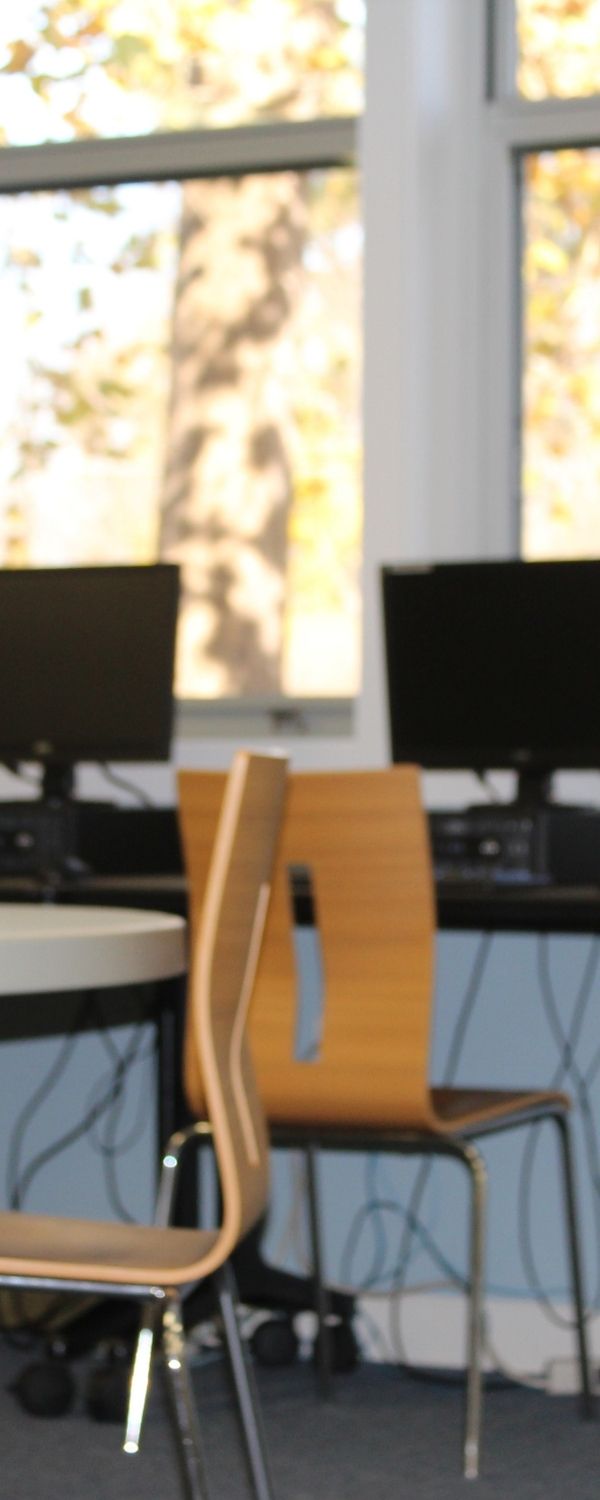 Picture of Community Center classroom with round tables and two chairs with computer stations in the background