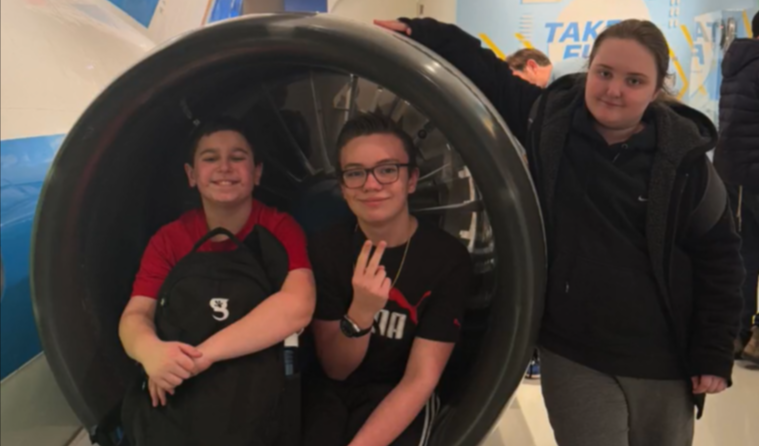 three kids sitting in a plane in a museum smiling