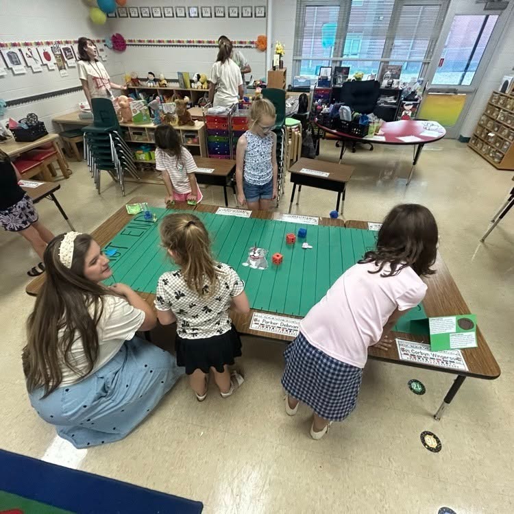 Students are working with with a teacher on math facts on a green football field