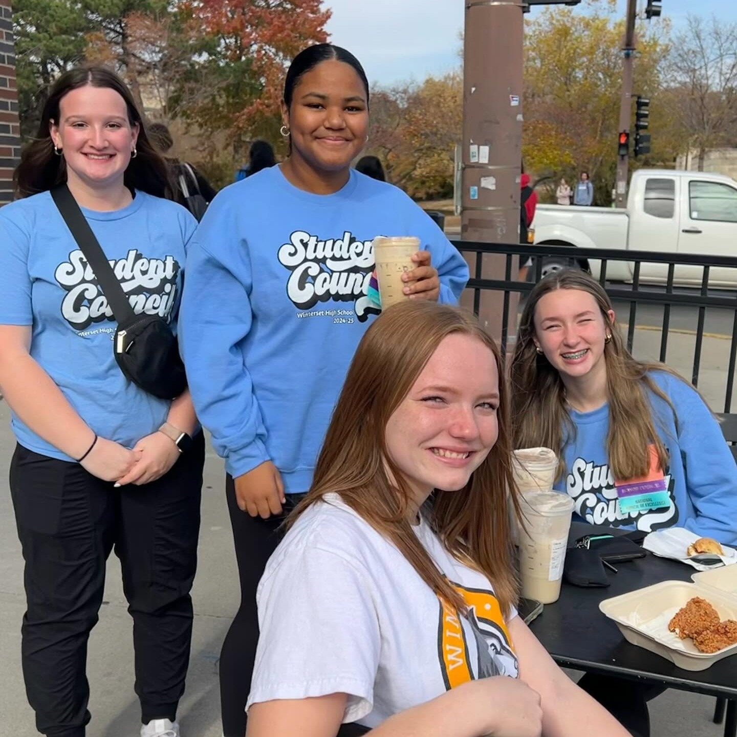 Four women in blue t-shirts standing outside a restaurant, with one holding a coffee cup.