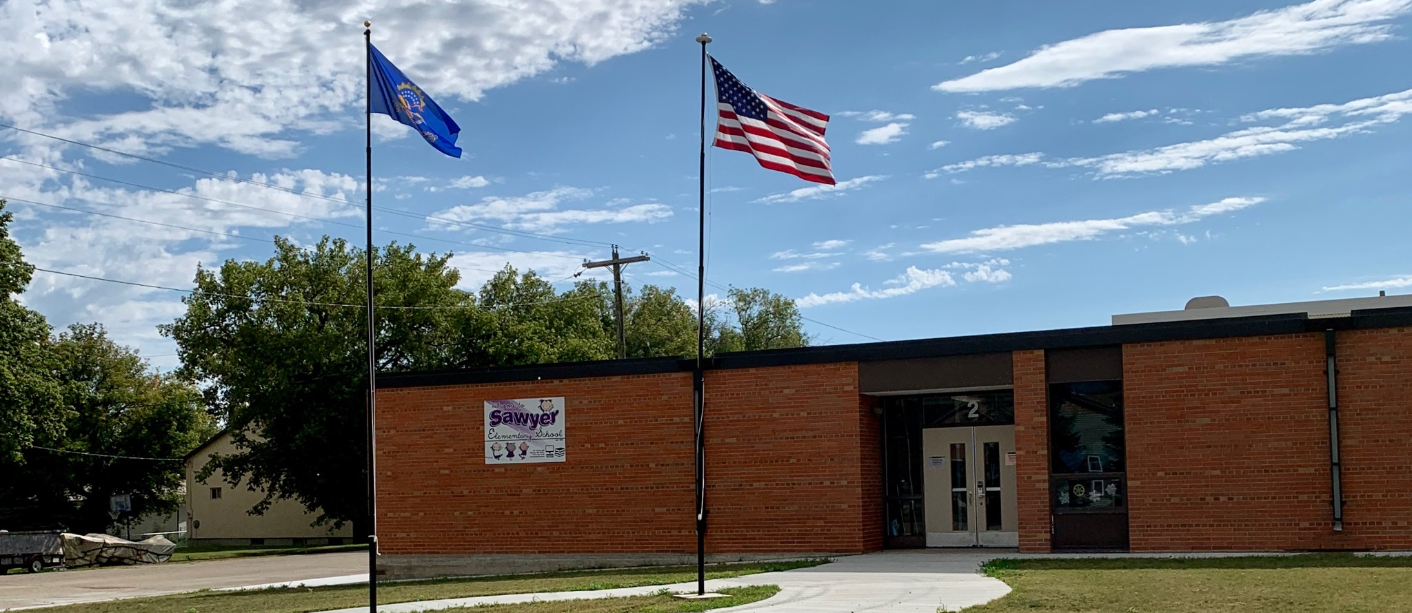 Outside view of Sawyer School with the United States flag and North Dakota flag waving patriotically in the wind.