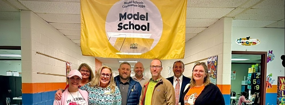 Educators pose in front of a model school banner