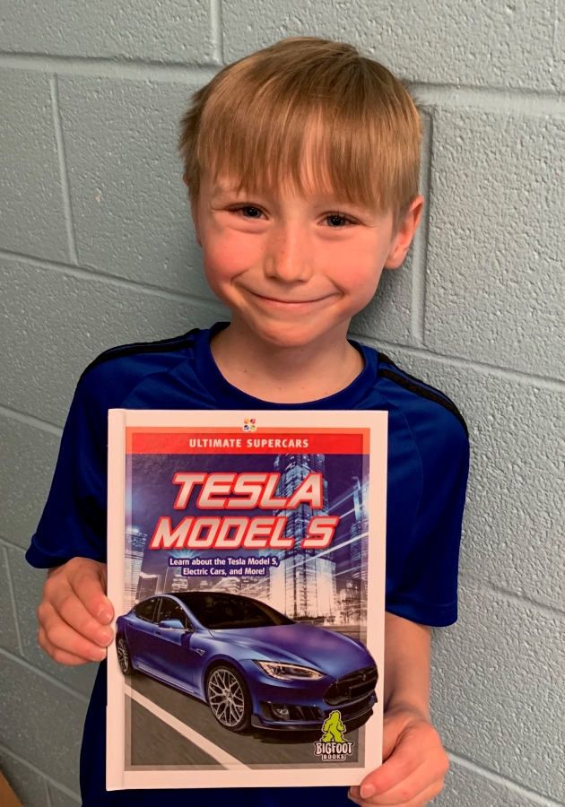 Student holding up a book of Tesla Models