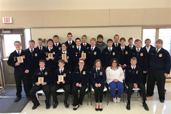 A group photo of a large number of students in formal attire, holding awards, posing together in a classroom setting.